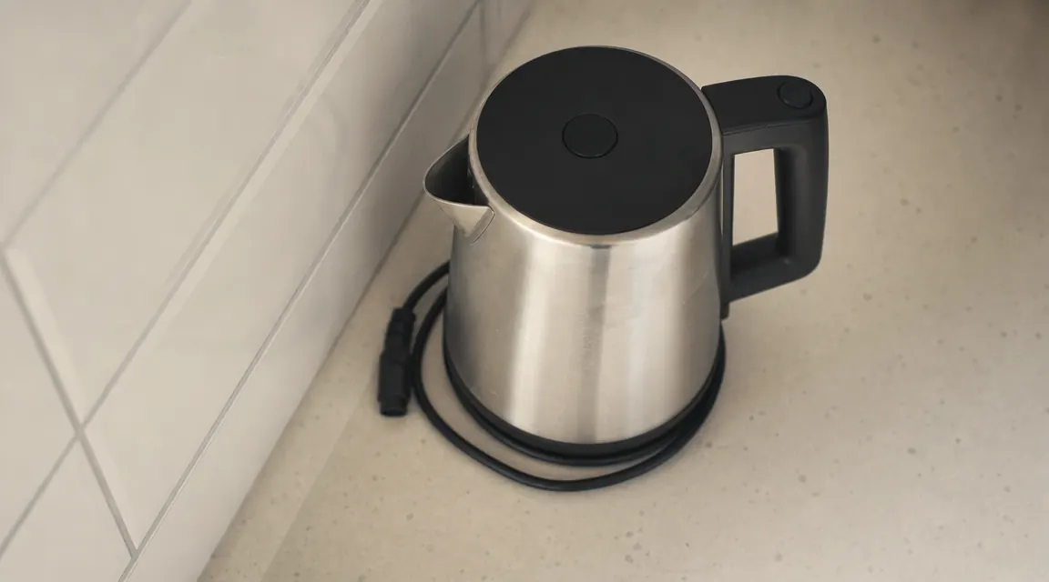 Short power cord coiled beside the base of an electric kettle on a counter near an outlet